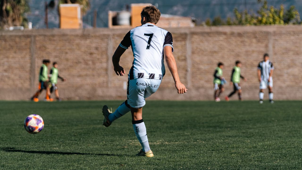 our-stories Soccer player in action on field during daytime match with teammates in background.