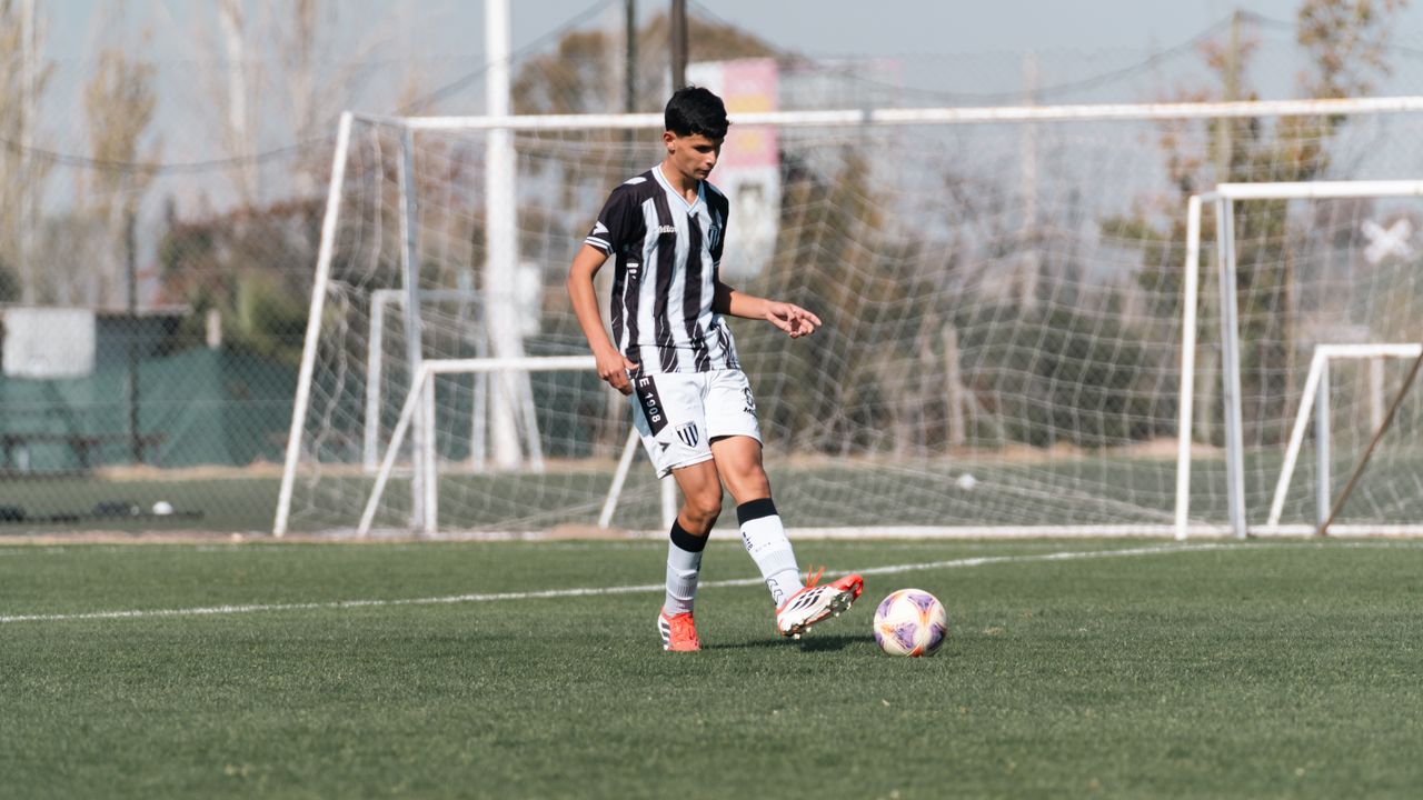 who-we-are A teenage soccer player dribbles the ball on an outdoor football field during the day.